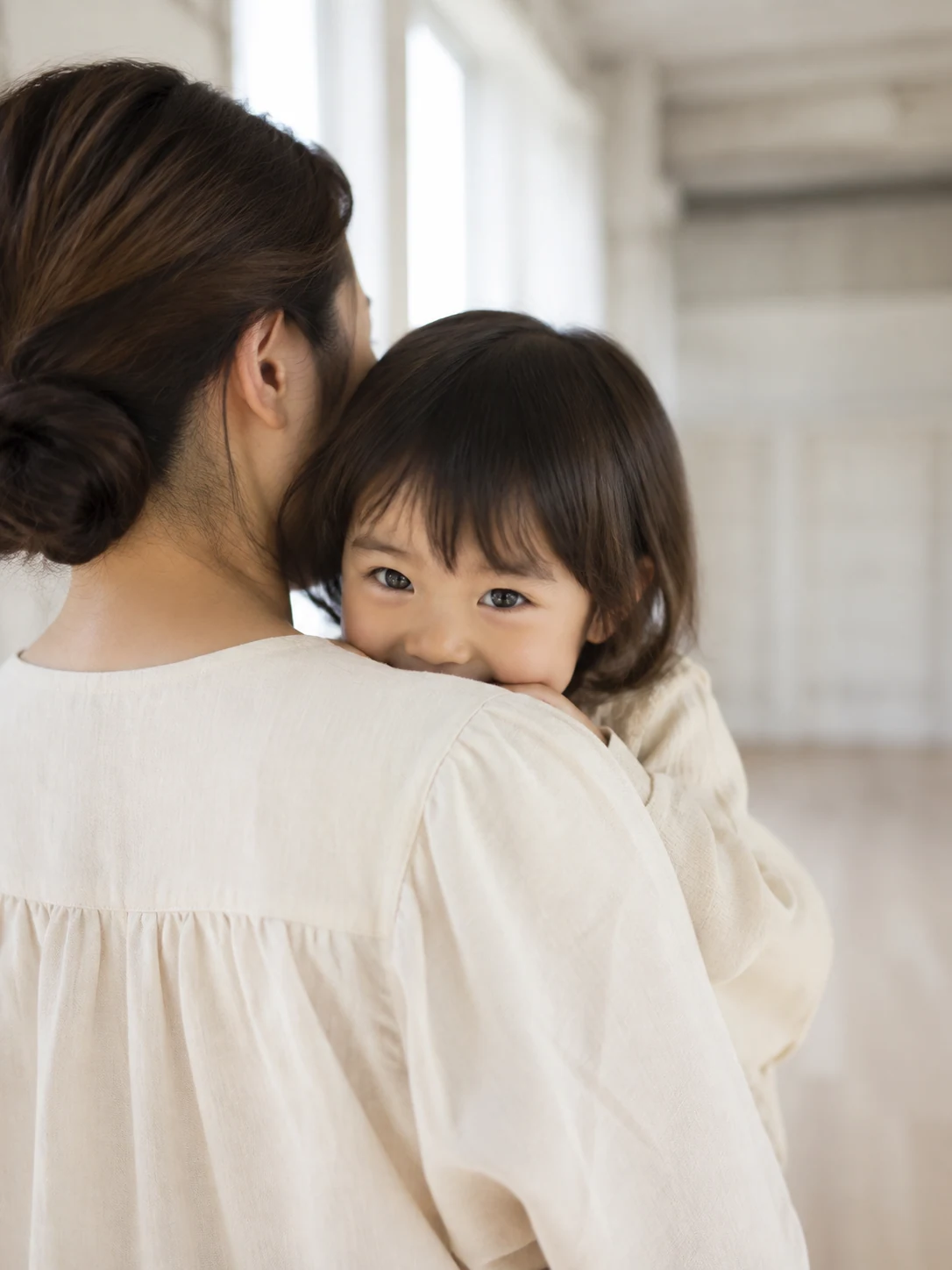 お母さんの肩から少しだけ顔をのぞかせる子ども