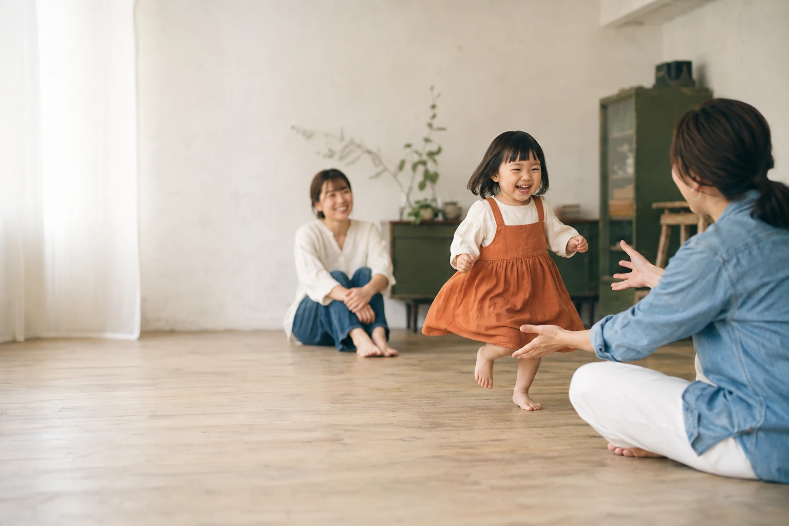オレンジ色の服の女の子が、床に座るスタッフに向かって笑顔で走る